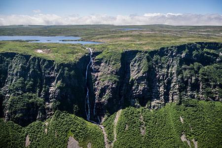 An aerial view of a deep gorge with a waterfall, above a wide plateau of lakes and open barrens.