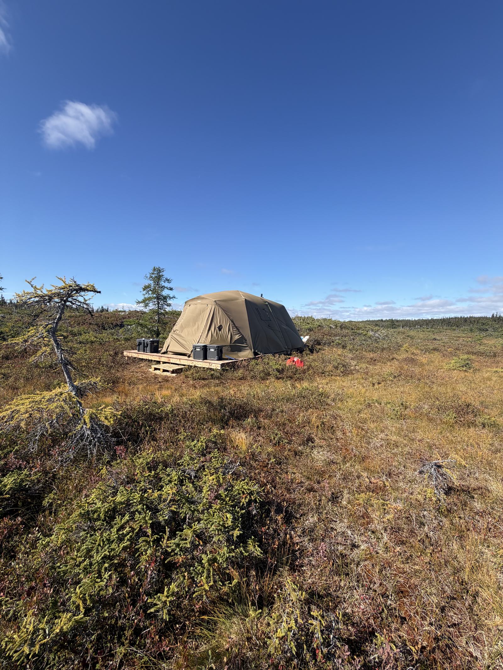 A single tent camp on open tundra under a deep blue sky.