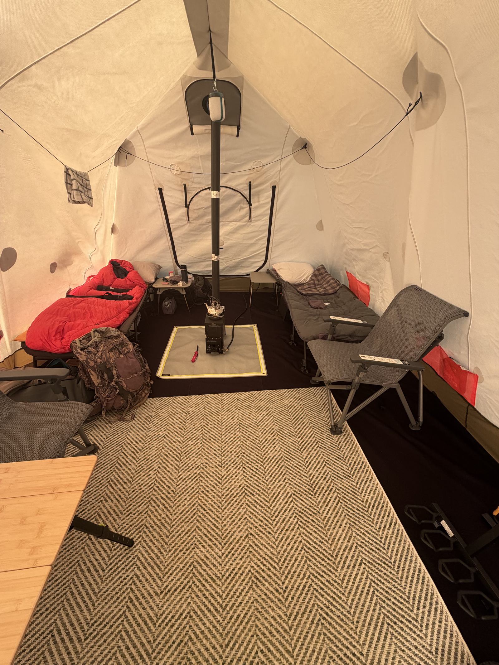 Inside a heated white tent: a wood stove, camp cots and a table laid out for the evening.